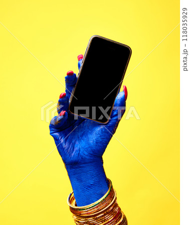 Witch's blue hand with vivid manicure holds smartphone with blank screen against yellow background. Negative space to insert text Witch's blue hand with vivid manicure holds smartphone with blank screen against yellow background. Negative space to insert text 118035929