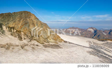 The Taschachferner Glacier showcases its expansive ice surface against a backdrop of rugged mountain peaks in the Otztal Alps. Clear blue skies enhance the breathtaking natural beauty of this alpine 118036009