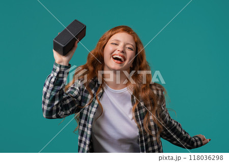 Cute woman listening music by wireless portable speaker, sound system on blue, dancing, enjoying rhythm. 118036298