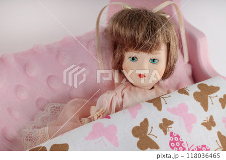 Close-up of a vintage doll with blue eyes resting on a pink bed with a butterfly-patterned blanket. Close-up of a vintage doll with blue eyes resting on a pink bed with a butterfly-patterned blanket. 118036465