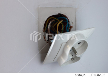 A close-up view of a faulty wall socket with exposed wiring, highlighting a dangerous electrical situation. A close-up view of a faulty wall socket with exposed wiring, highlighting a dangerous electrical situation. 118036496