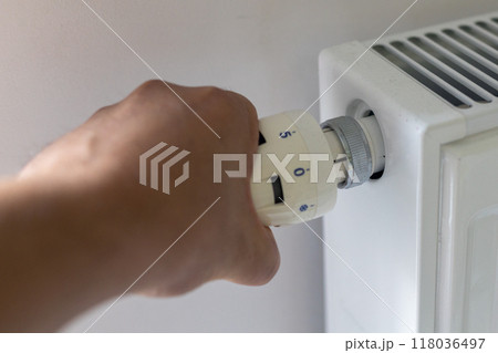 Hand turning the thermostat on a radiator to control temperature. 118036497