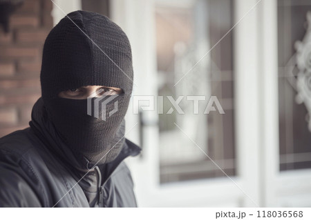 Close-up of a masked intruder wearing a black balaclava, staring intently at the camera. 118036568