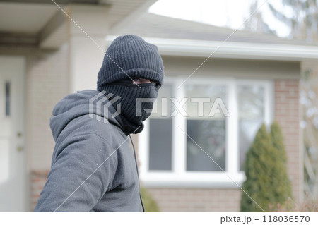 A man in a black mask stands outside a suburban house, looking towards the camera. A man in a black mask stands outside a suburban house, looking towards the camera. 118036570