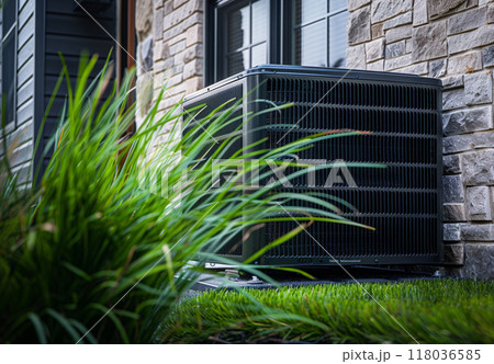 A close-up of an outdoor air conditioning unit installed beside a modern stone wall with greenery in the foreground. 118036585