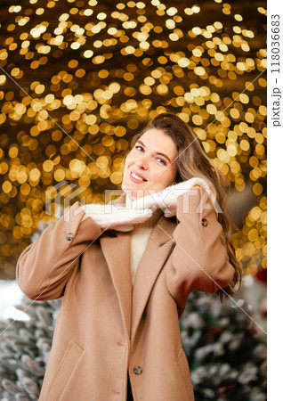 happy woman in a coat and white mittens stands in front of Christmas garlands, holiday mood 118036683