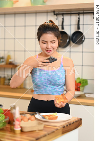 Happy young woman taking photo of her breakfast on wooden kitchen counter with smartphone Happy young woman taking photo of her breakfast on wooden kitchen counter with smartphone 118036874