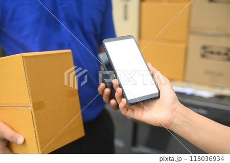 Woman making contactless payment with phone and received package from courier. Shipping and delivery services concept Woman making contactless payment with phone and received package from courier. Shipping and delivery services concept 118036934