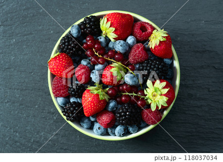 Mix of ripe colorful berries in bowl photography . Blueberry , strawberry , raspberry , blackberry and red currant . Top view 118037034