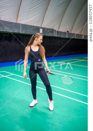 Sports young woman with racket and shuttlecock is posing before playing in badminton on inside court Sports young woman with racket and shuttlecock is posing before playing in badminton on inside court 118037457