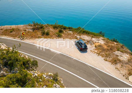 Car with a roof box, parked on the edge of a cliffside road, with the azure sea below reflecting the clear blue sky.  118038228