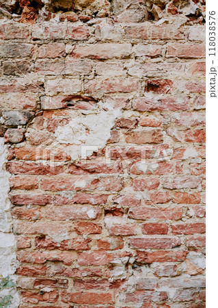 Detail of an aged brick wall with cracked, peeling plaster revealing underlying red and white bricks. The texture of the wall shows signs of erosion and structural wear Detail of an aged brick wall with cracked, peeling plaster revealing underlying red and white bricks. The texture of the wall shows signs of erosion and structural wear 118038576