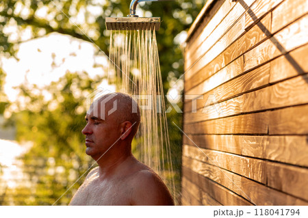 Man taking refreshing outdoor shower at sunset. Concept of relaxation and wellness 118041794