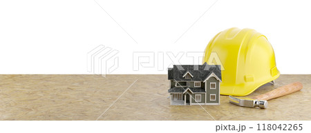 Miniature Model House, Yellow Construction Hard Hat and Hammer Resting on Particleboard Banner Isolated on a White Background. 118042265
