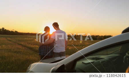 Married family couple in love hugging at sunset by car, romantically spending quiet time together, relaxing outside car. Husband and wife, spouses hugging, standing in field by car. Road trip, travel Married family couple in love hugging at sunset by car, romantically spending quiet time together, relaxing outside car. Husband and wife, spouses hugging, standing in field by car. Road trip, travel 118042615