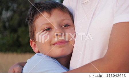Happy child boy snuggles up to mother, hugging at nature field. Mother parent woman embracing hugging kid child, mom cuddling with boy. Close up, face of smiling kid child enjoying mother gentle arms Happy child boy snuggles up to mother, hugging at nature field. Mother parent woman embracing hugging kid child, mom cuddling with boy. Close up, face of smiling kid child enjoying mother gentle arms 118042638