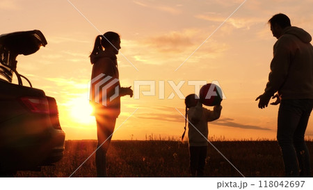 Family playing with ball near car at sunset, silhouettes. Father, mother, daughter throwing ball in circle, laughing, having fun joyful good time in field, creating pleasant unforgettable memories. Family playing with ball near car at sunset, silhouettes. Father, mother, daughter throwing ball in circle, laughing, having fun joyful good time in field, creating pleasant unforgettable memories. 118042697