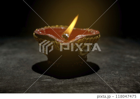 A red and gold decorated pot with a blue and white design sits on a dark surface 118047475