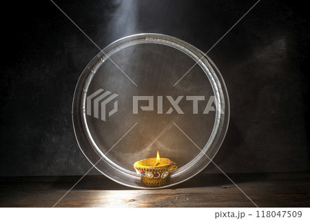Diya oil lamp on the sieve. The candle is lit and the light is shining through the mesh Diya oil lamp on the sieve. The candle is lit and the light is shining through the mesh 118047509