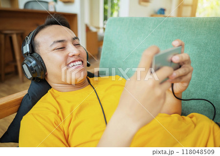An Indonesian man in a yellow shirt is smiling while playing a video game on his phone An Indonesian man in a yellow shirt is smiling while playing a video game on his phone 118048509