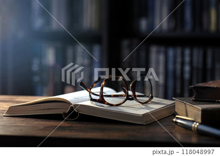アンティークな木のテーブルの上にある開かれた本、眼鏡 118048997