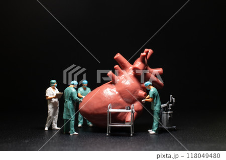 Miniature medical professionals performing a procedure on a large heart model. 118049480