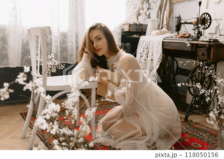 Young caucasian lady wearing vintage bridal dress sitting on floor at home in stylish vintage interior 118050156
