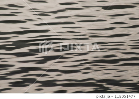 A calm, wavy water surface. A peaceful image of a calm water surface. Ideal for creating a natural and minimalist atmosphere. A fascinating image formed by the reflections of a calm water surface. 118051477