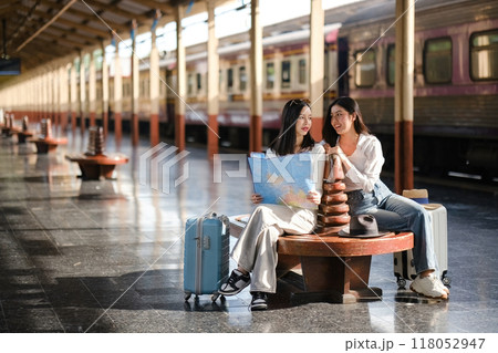 Two women sitting on a bench with suitcases and a map Two women sitting on a bench with suitcases and a map 118052947