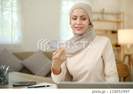 A woman wearing a hijab is holding a credit card in front of a laptop 118052997
