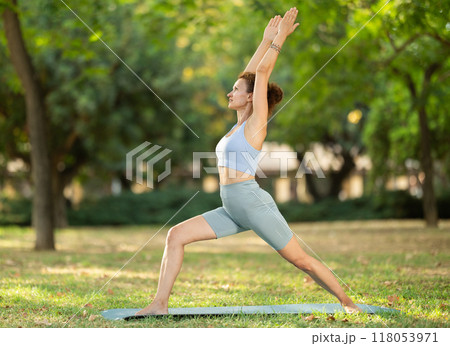Woman practicing yoga in garden, performing Anjaneyasana, or Crescent Moon Pose 118053971