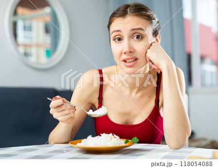 Sad woman eating rice while sitting at the table in the room. Diet concept and diet foods 118054088
