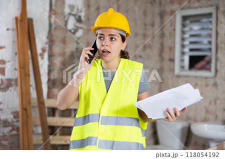 Young woman civil engineer with papers talking on phone at construction site 118054192