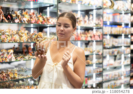 Female tourist happily chooses souvenir figurine of an eagle owl in Spanish souvenir shop 118054278