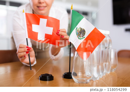 Woman secretary prepares an office for negotiations - she places flags of Switzerland and Mexico table Woman secretary prepares an office for negotiations - she places flags of Switzerland and Mexico table 118054299