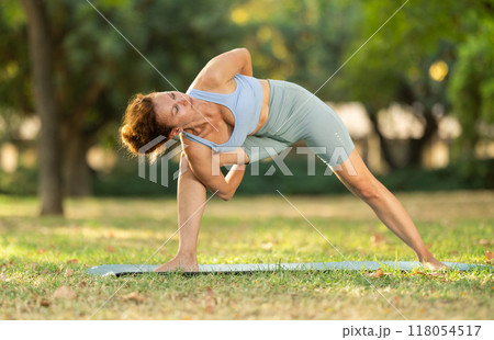 Woman practicing yoga in garden, performing Anjaneyasana, or Crescent Moon Pose Woman practicing yoga in garden, performing Anjaneyasana, or Crescent Moon Pose 118054517