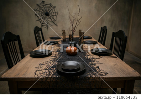 Eerie Halloween table setting with black plates, candles, spiderweb decor on dimly lit background. Spooky dining concept Eerie Halloween table setting with black plates, candles, spiderweb decor on dimly lit background. Spooky dining concept 118054535