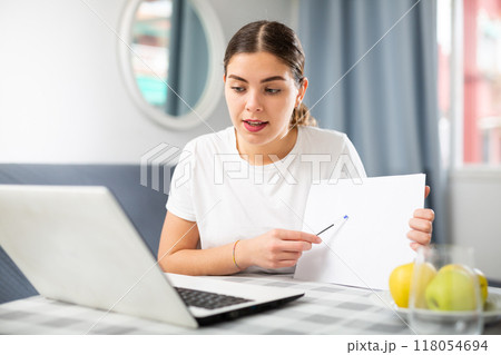 Woman studying via internet using laptop while sitting at table at home 118054694