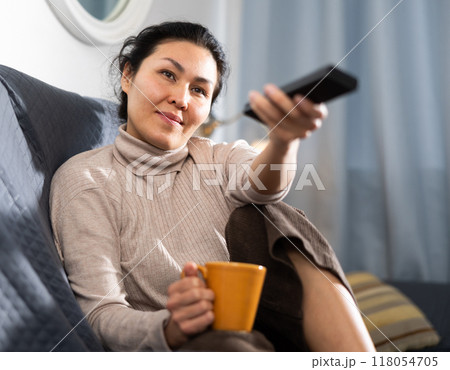 Woman holding cup of coffee and watching TV at home Woman holding cup of coffee and watching TV at home 118054705