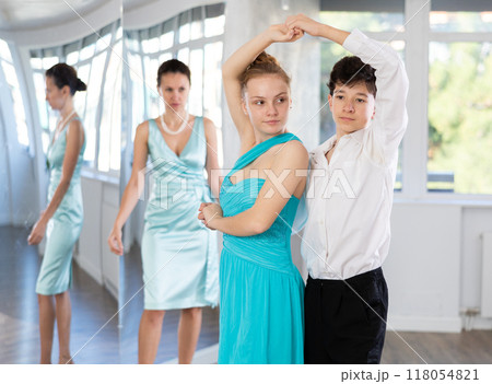 Couple of teenagers in festive clothes learn to dance latin american dance Bachata in studio under the guidance of teacher 118054821
