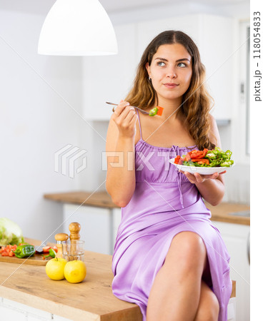 Portrait of positive woman in nightdress eating salad at home Portrait of positive woman in nightdress eating salad at home 118054833
