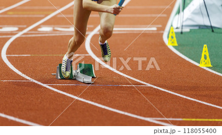 Athlete in sprinting shoes launches off the starting blocks during a competitive track race on an indoor arena surface Athlete in sprinting shoes launches off the starting blocks during a competitive track race on an indoor arena surface 118055400