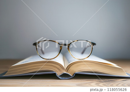 Open book resting on a wooden table, with eyeglasses laying on top of the open pages. Generative AI 118055626