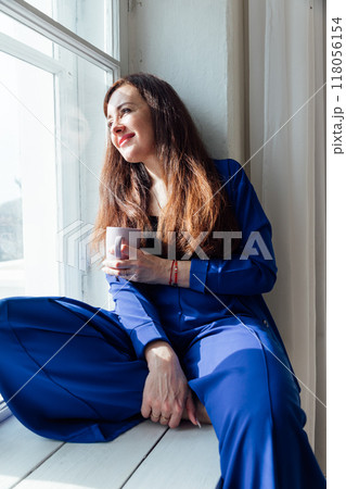 Woman Brunette In Blue Suit Sitting By Window Looking Woman Brunette In Blue Suit Sitting By Window Looking 118056154