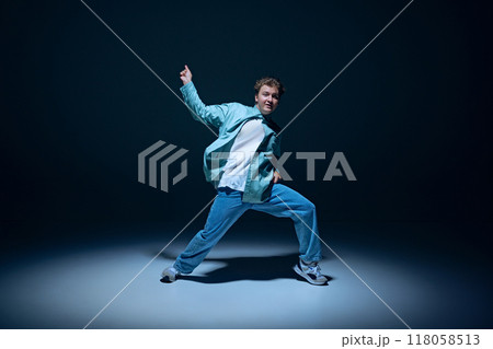 Stylish young guy, hip-hop dancer in motion on stage, training, performing with energy against navy blue background 118058513