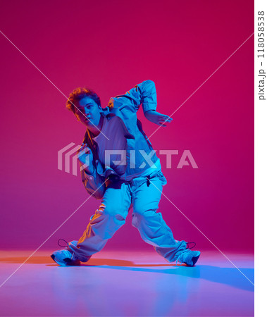 Dance club member. Young energetic man in casual clothes in motion, dance hip hop against pink background in neon light Dance club member. Young energetic man in casual clothes in motion, dance hip hop against pink background in neon light 118058538