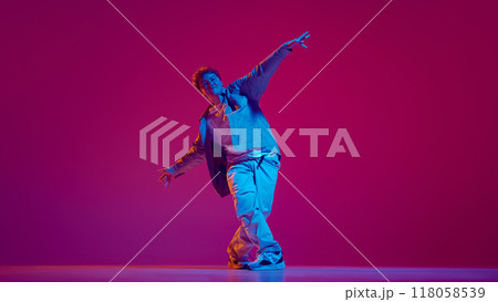 Dynamic image for young artistic and talented man in casual clothes performing hip-hop, training against pink background in neon light 118058539
