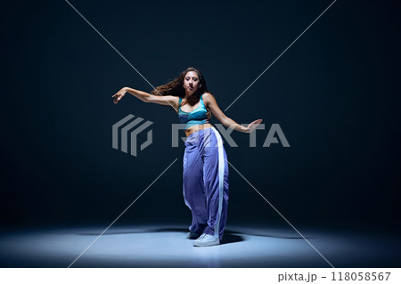 Dynamic image of young girl, dancer showing technique during focused hip hop training session against navy blue studio background 118058567