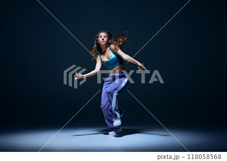 Dynamic image of young girl, dancer showing technique during focused hip hop training session against navy blue studio background 118058568