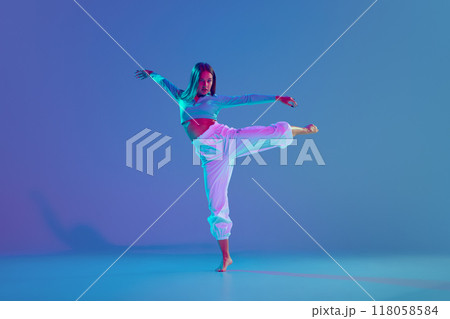 Dance club member. Young talented and expressive girl, dancer making energetic hip hop performance against gradient blue background in neon light 118058584